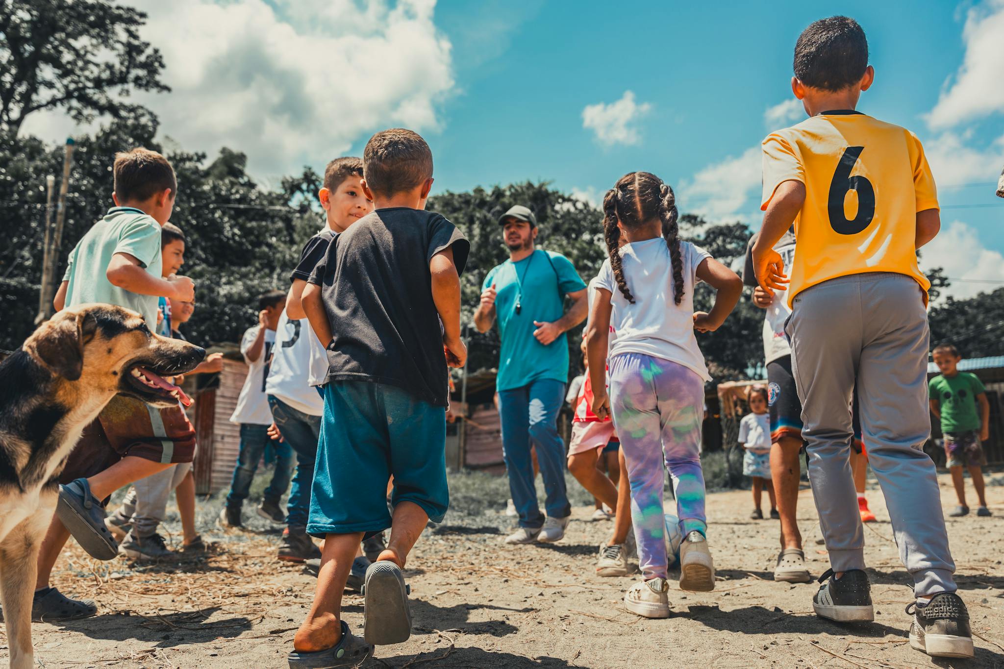 Group of children playing in a field under supervision, enjoying a sunny day outdoors.