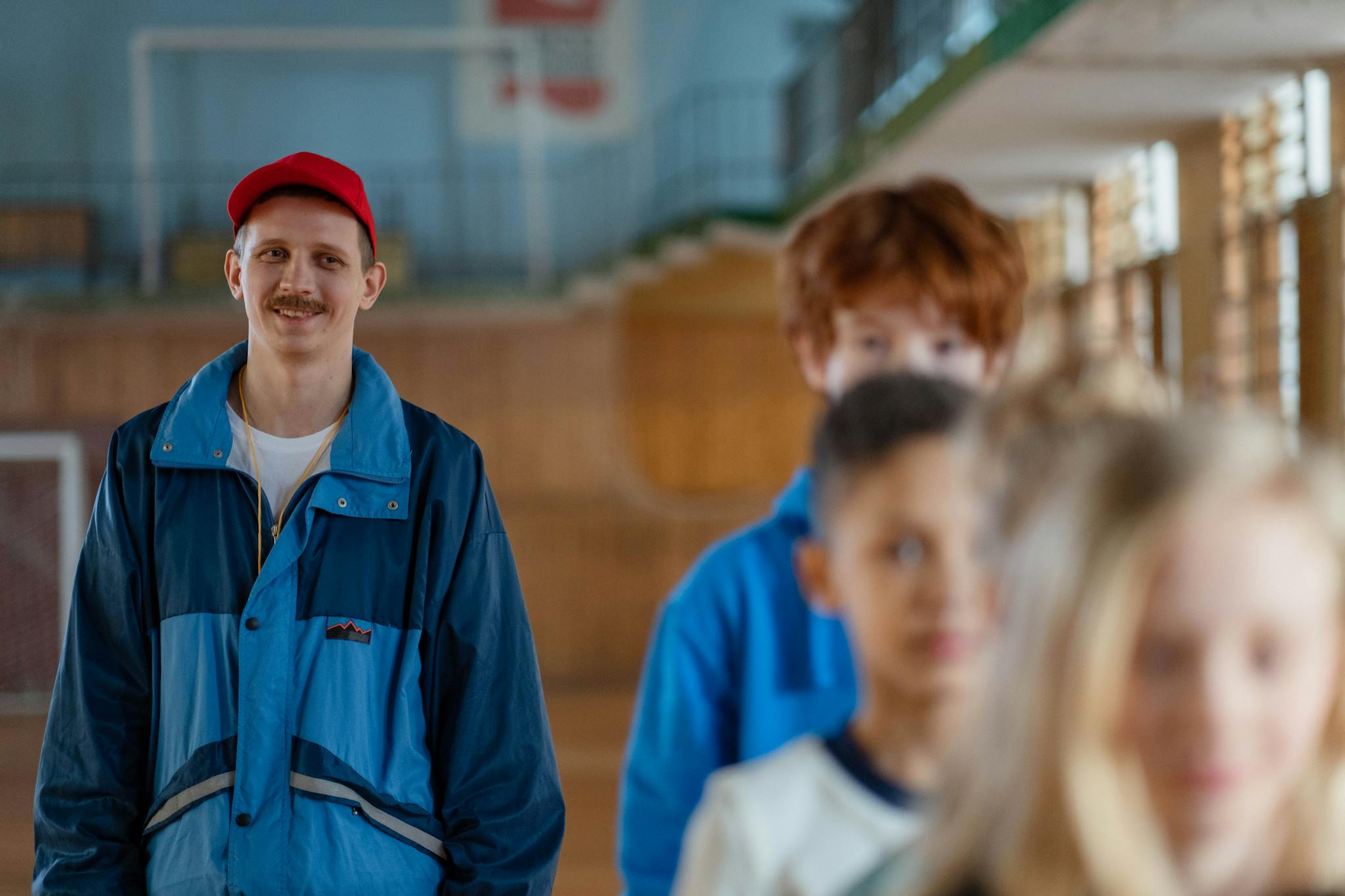 Smiling male coach guiding children in a gym setting during a physical education class.